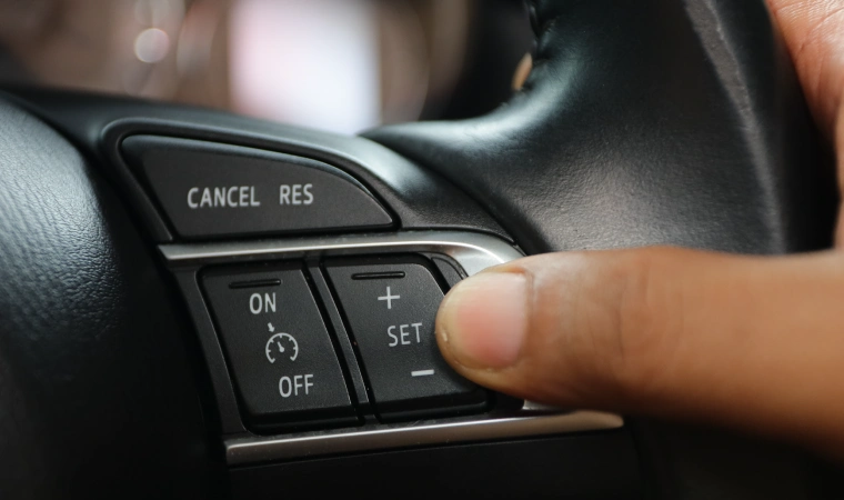 Finger pressing the 'set' button on a steering wheel for adaptive cruise control.